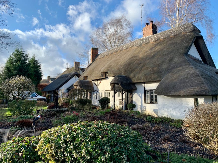 Idyllic thatched roof cottage surrounded by lush garden on a sunny day.
