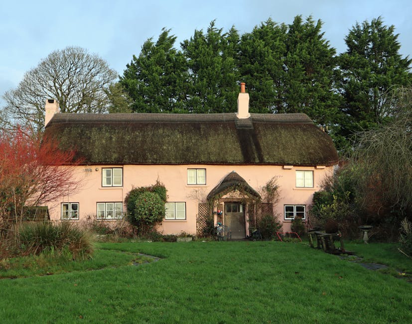 A beautiful pink thatched-roof cottage nestled in serene countryside with lush greenery.